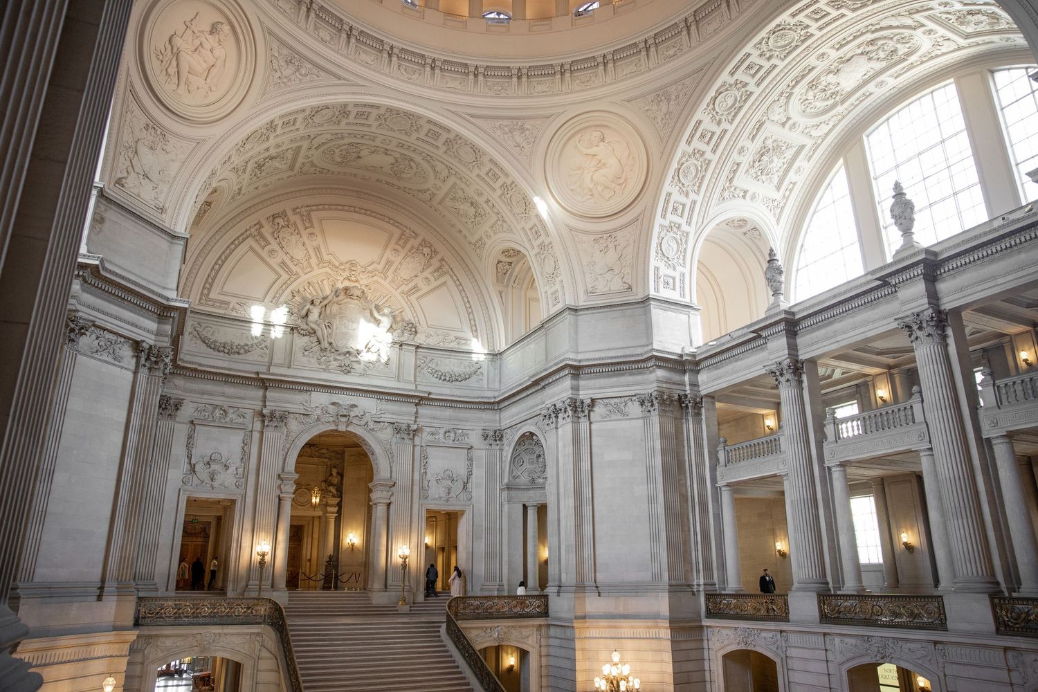 Grand interior of San Francisco City Hall featuring ornate Beaux-Arts architecture, sweeping staircase, and elegant rotunda dome.