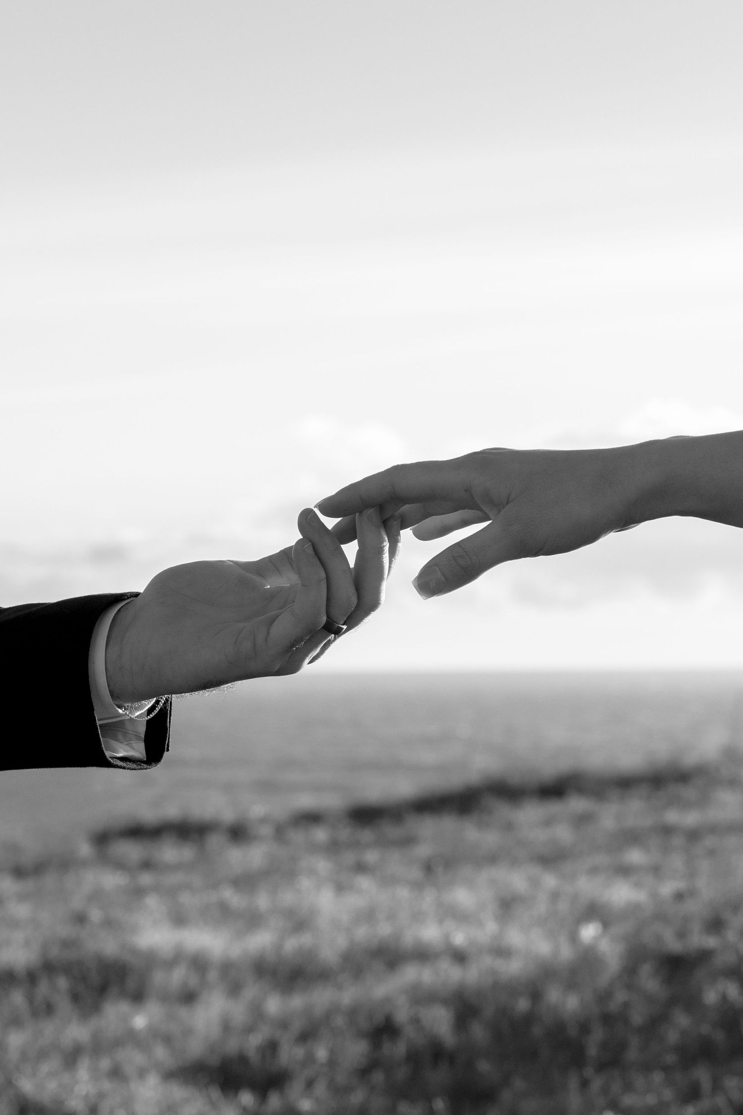 Two hands reaching toward each other outdoors, evoking romance and connection in black and white.
