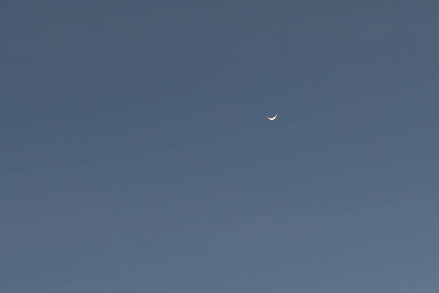 Crescent moon against a dusky blue sky at Shark Fin Cove in Davenport, California.