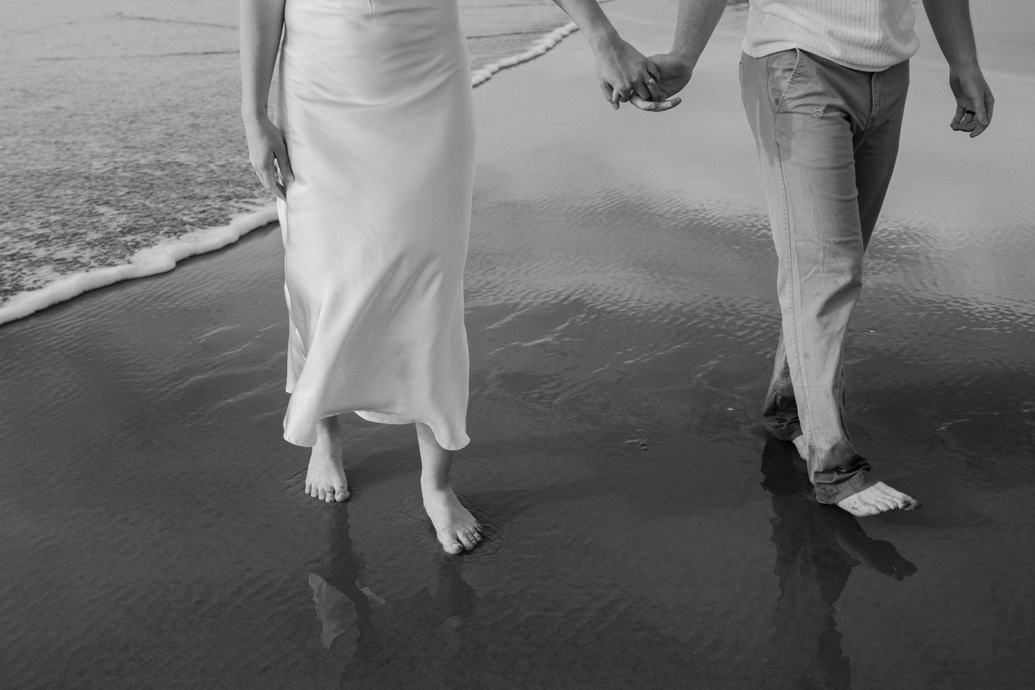 A barefoot couple holding hands while walking on a wet sandy beach in Oregon in black and white by Taylor Zimmerman Photo