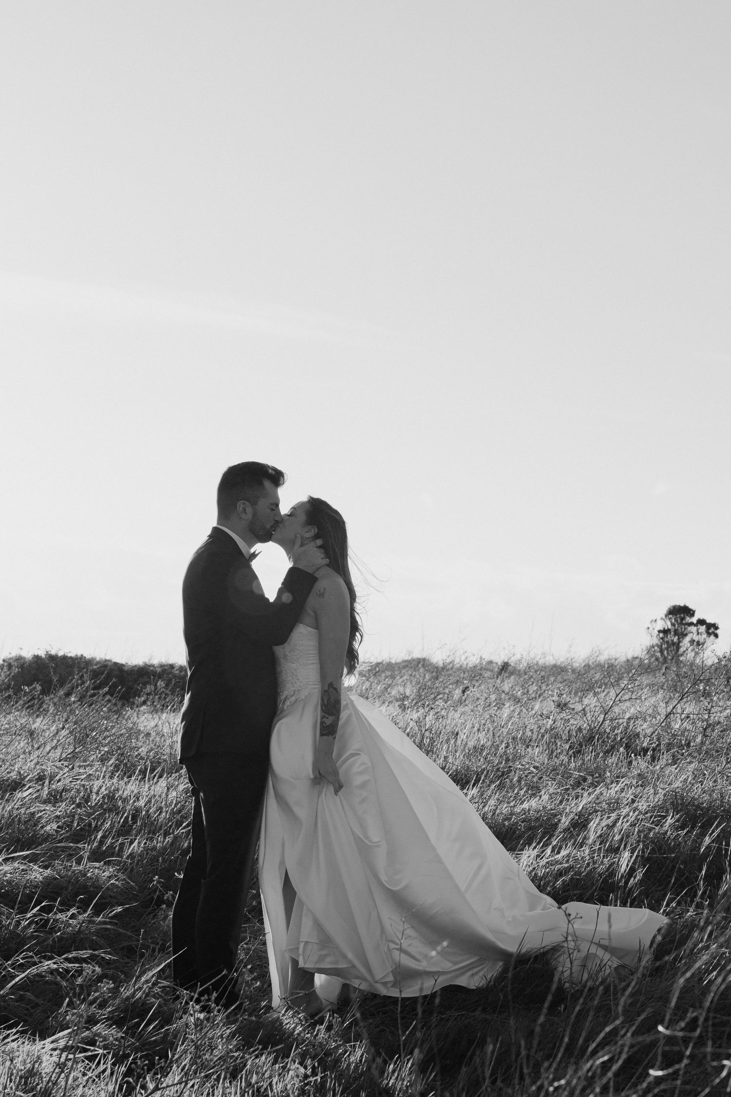 Bride and groom sharing a romantic kiss in a grassy field on their wedding day in black and white.