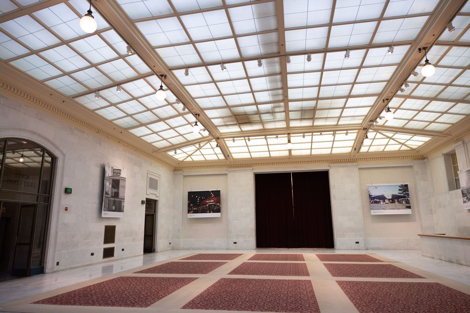 Elegant art gallery interior with skylight ceiling, patterned rugs, and paintings displayed on white walls inside of San Francisco City Hall