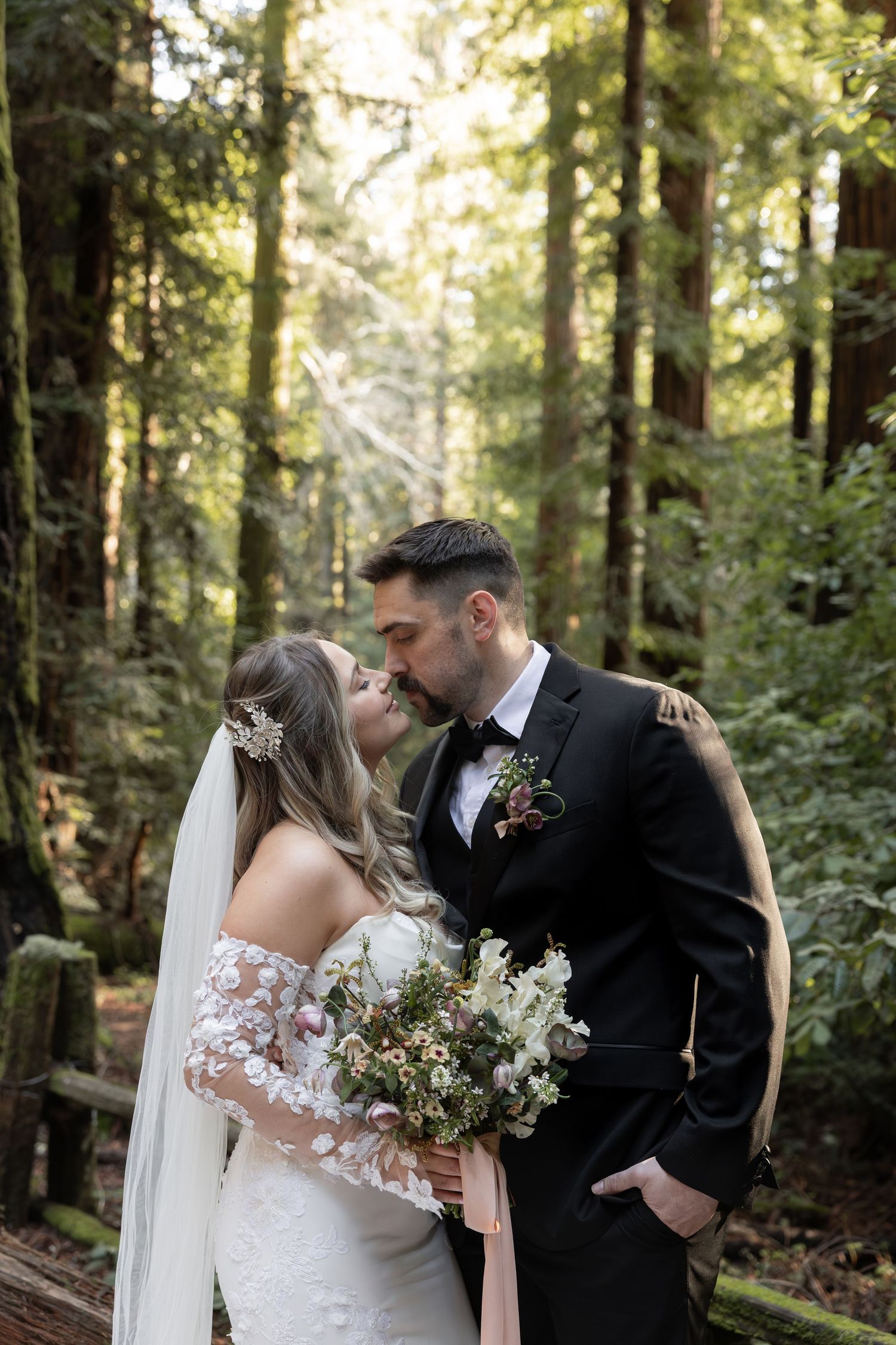 Bride and groom kiss in a sunlit redwood forest, bride holding a bouquet by Taylor Zimmerman Photo