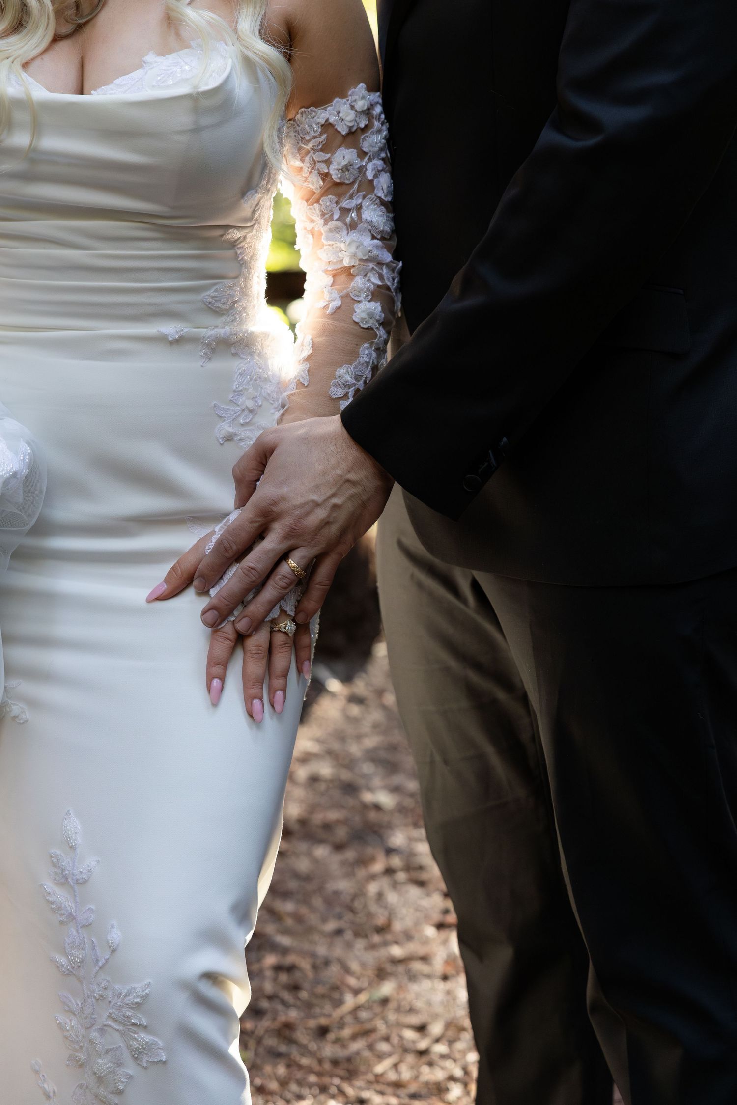 Bride and groom holding hands showing wedding rings, bride in white lace gown beside groom in dark suit by Taylor Zimmerman Photo