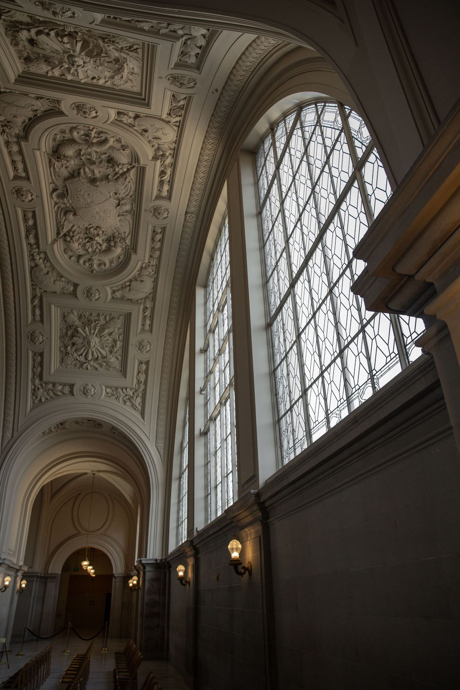 Grand interior hall with ornate carved ceiling, tall arched windows, and wall sconces inside San Francisco City Hall.