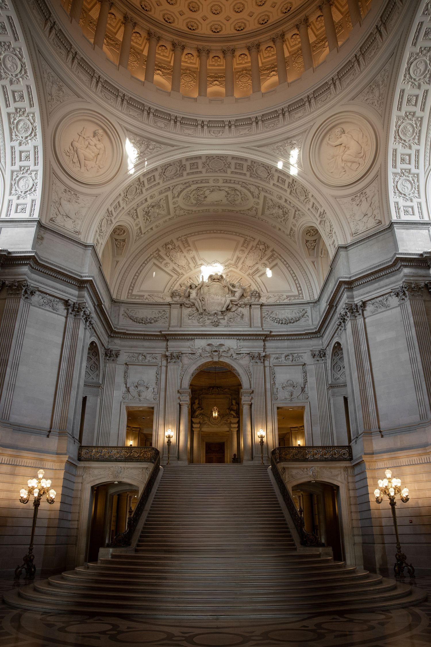 Grand interior staircase of San Francisco City Hall with ornate dome, classical columns, and elegant chandeliers.