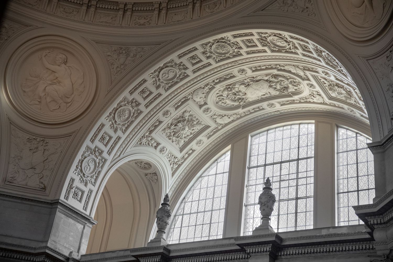Ornate neoclassical ceiling arch with intricate plasterwork reliefs and large arched windows inside San Francisco City Hall.