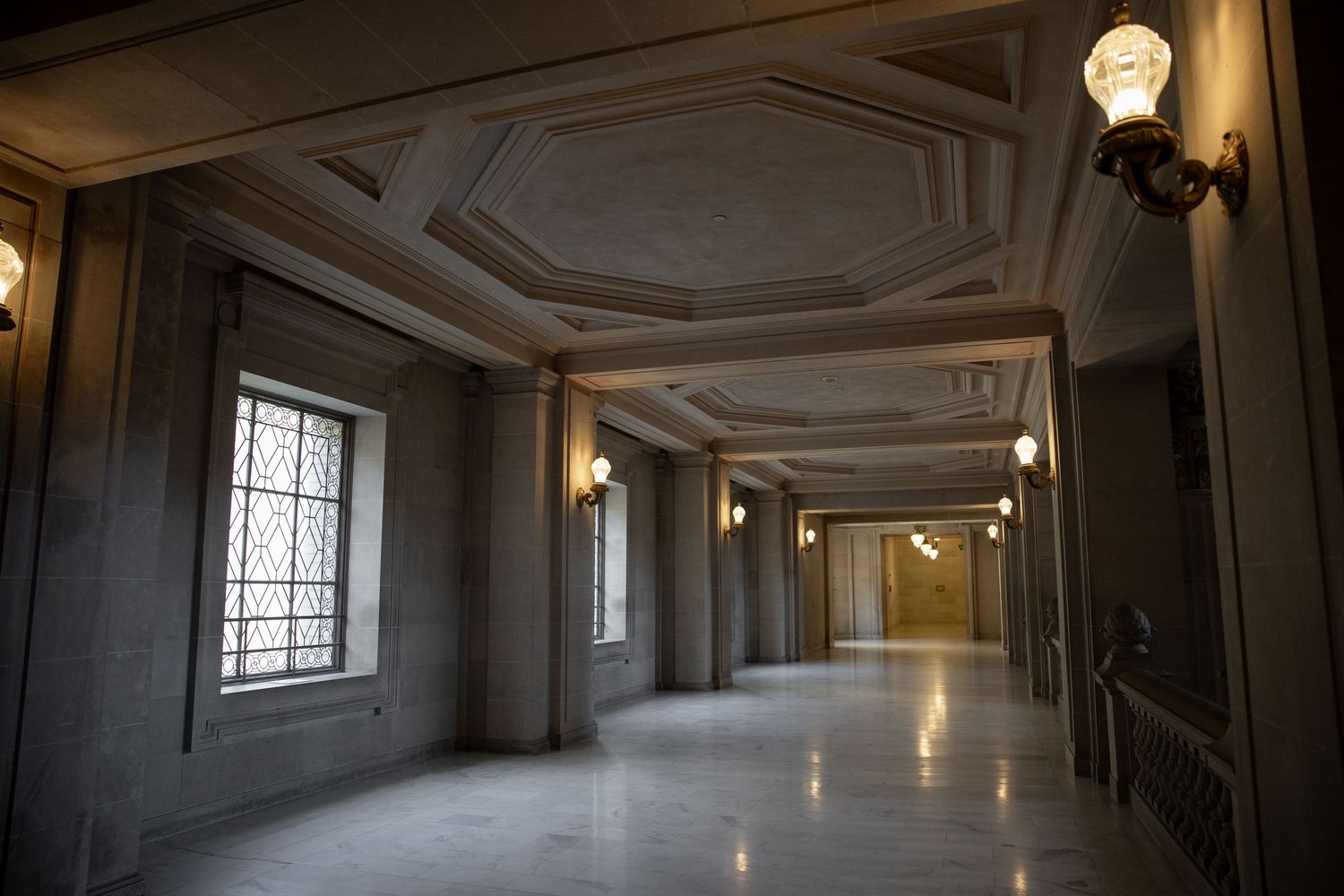 Elegant marble hallway with ornate coffered ceiling, wall sconces, and tall windows inside San Francisco City Hall.