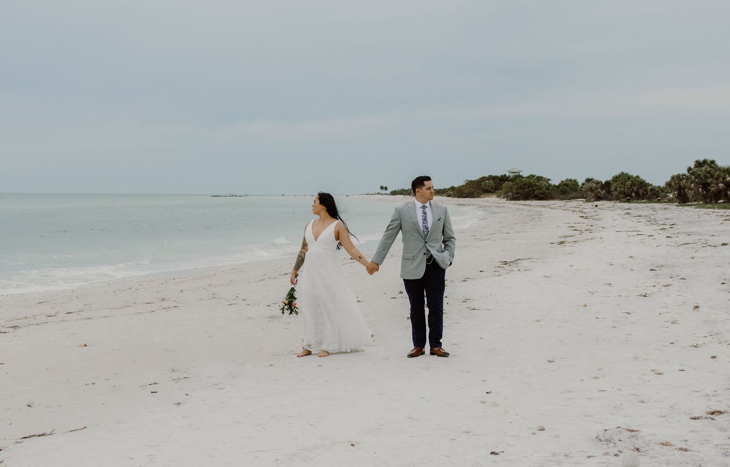 Bride and groom holding hands and pose on a white sand beach in Florida with calm ocean waters in the background by Taylor Zimmerman Photo