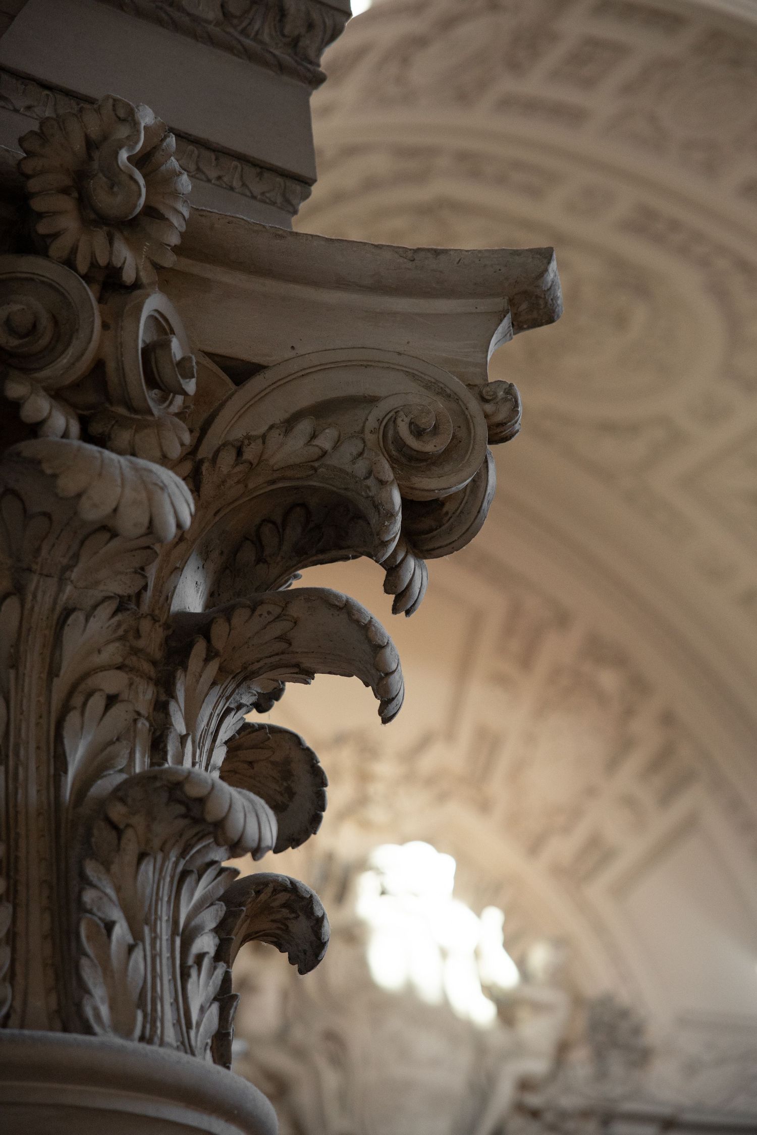Close-up of ornate Corinthian column capital with acanthus leaf carvings inside a baroque architectural interior.