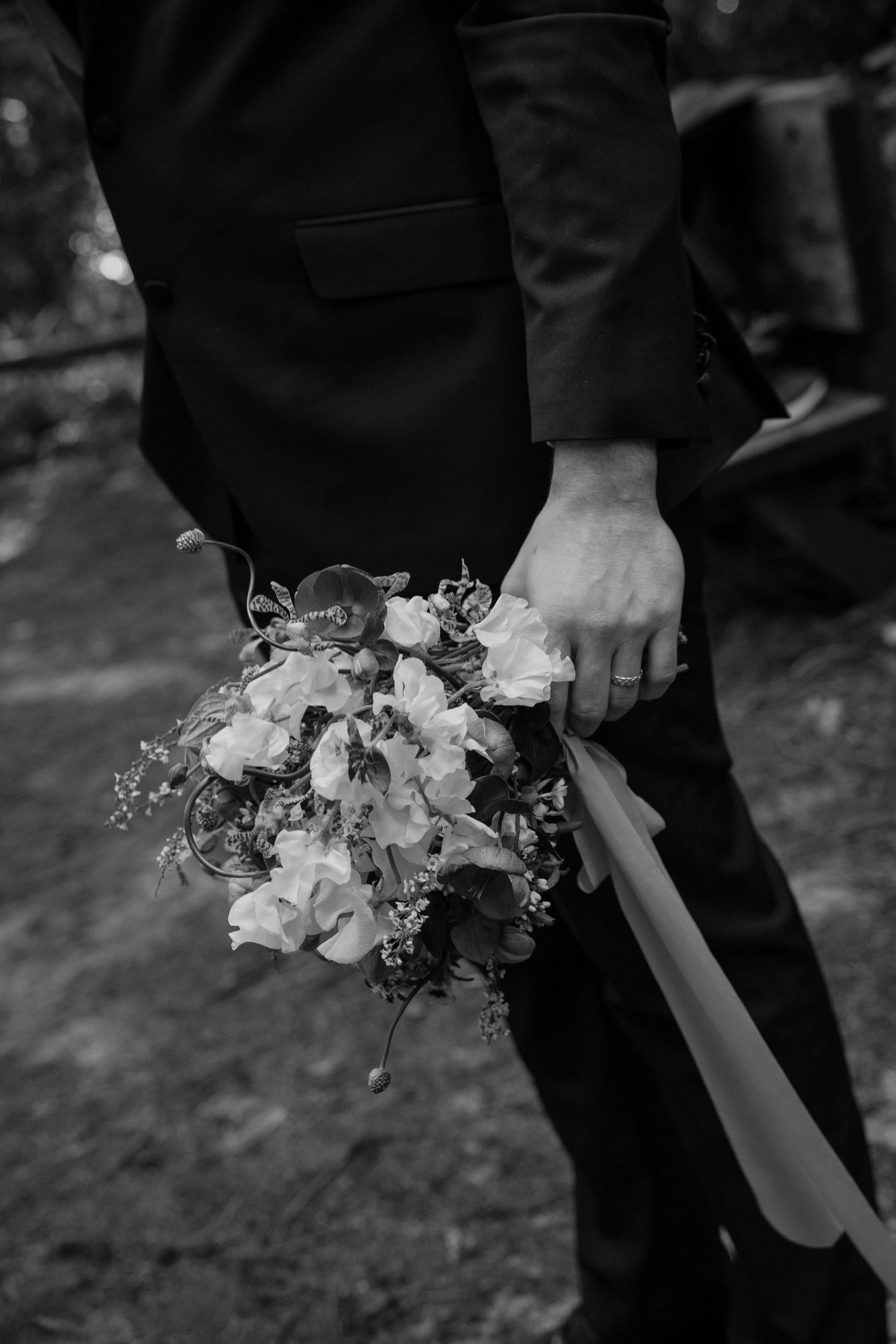 Groom holding a bridal bouquet of white flowers and ribbons in black and white by Taylor Zimmerman Photo