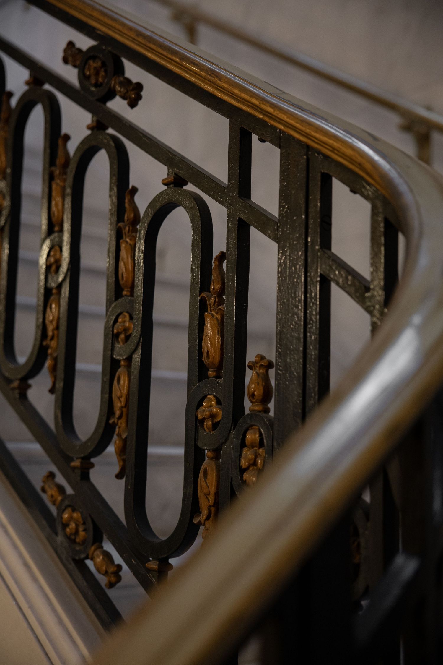 Ornate wrought iron staircase railing with gold decorative accents and wooden handrail inside San Francisco City Hall.
