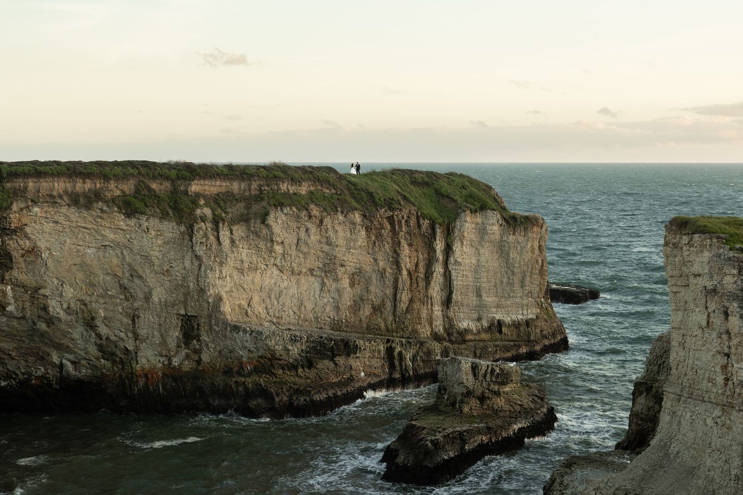 Wide view of couple walking on top of the cliffs at Shark Fin Cove along the Northern California coast.