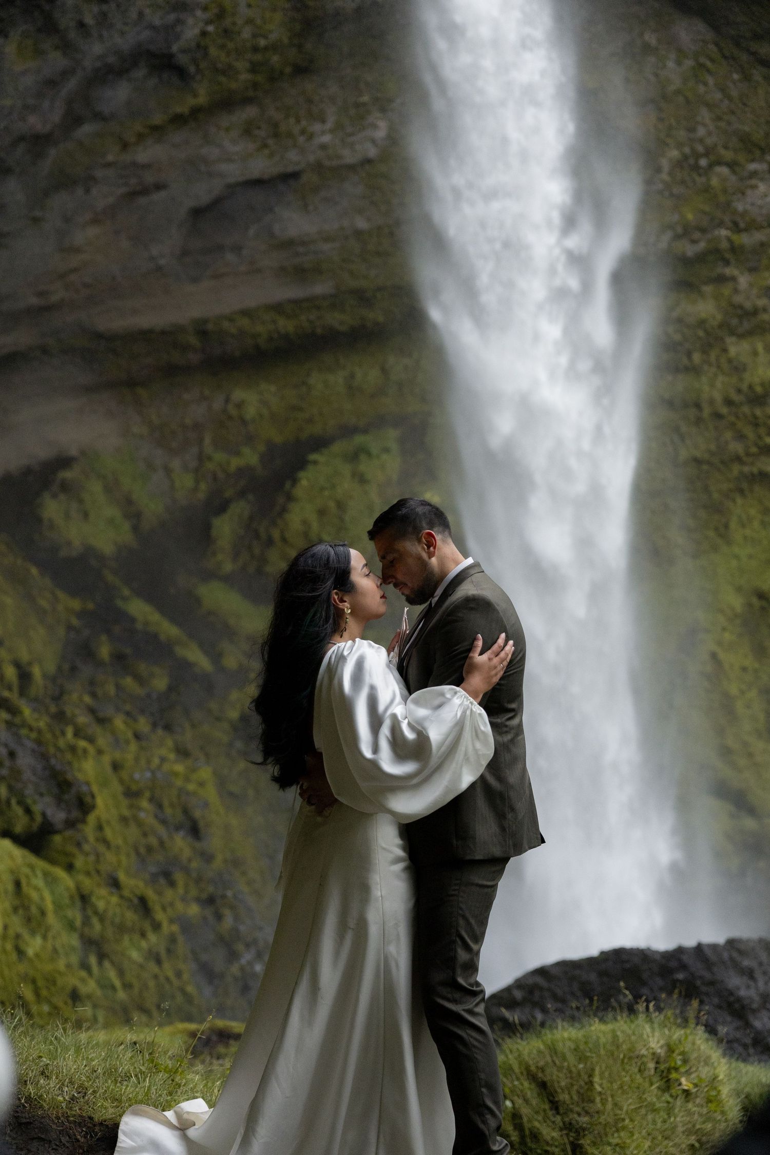 A bride and groom gently touch foreheads in front of a waterfall during their elopement in Iceland by Taylor Zimmerman Photo