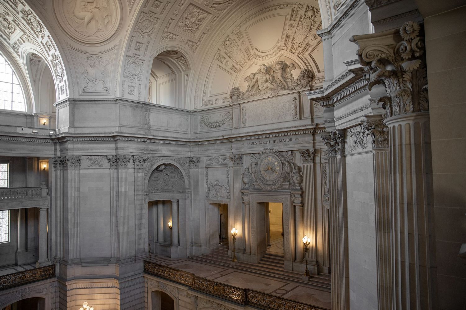 Grand interior of San Francisco City Hall featuring ornate Beaux-Arts architecture, marble columns, and elaborate ceiling details.