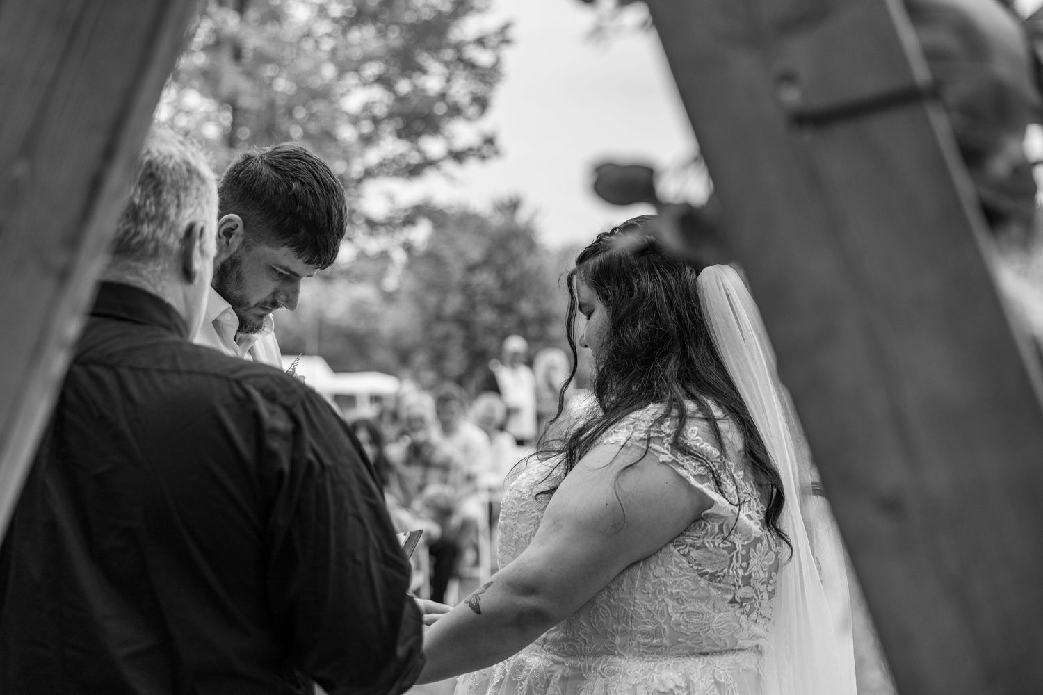 Bride and groom hold hands during an intimate outdoor wedding ceremony beneath a wooden arch.