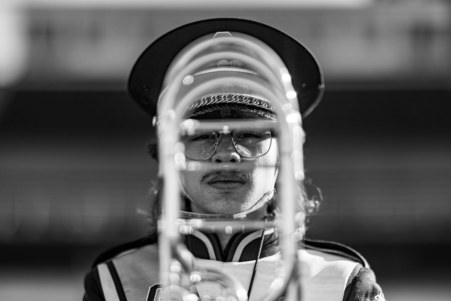 Black and white close-up of musician peering through brass instrument bell wearing hat.
