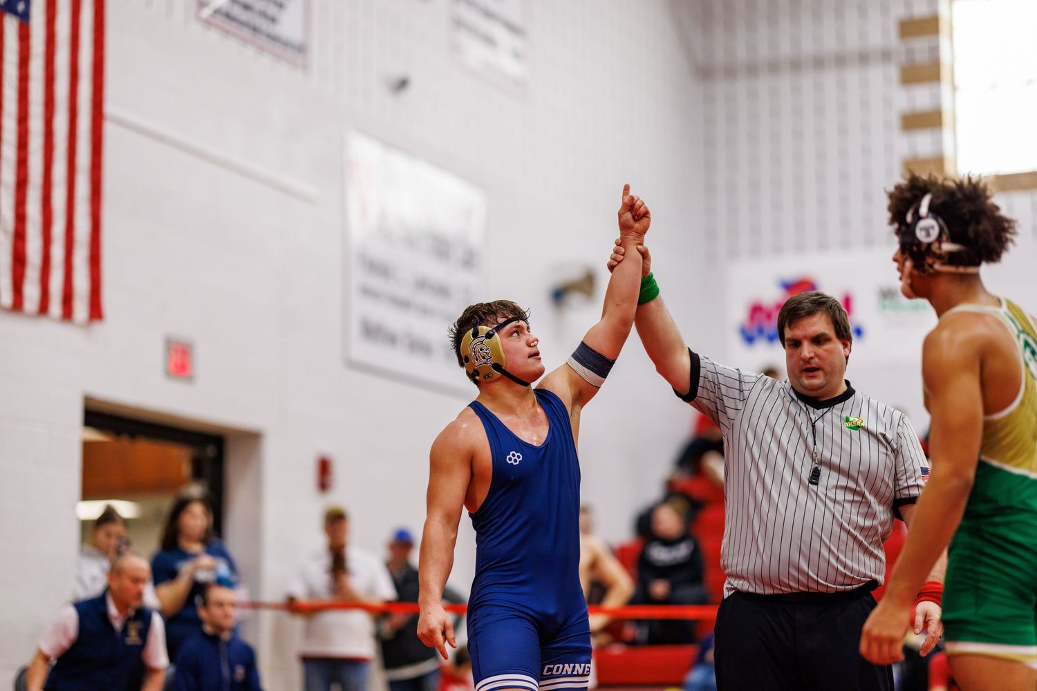 A referee raises a wrestler's hand in victory during a high school wrestling tournament match.