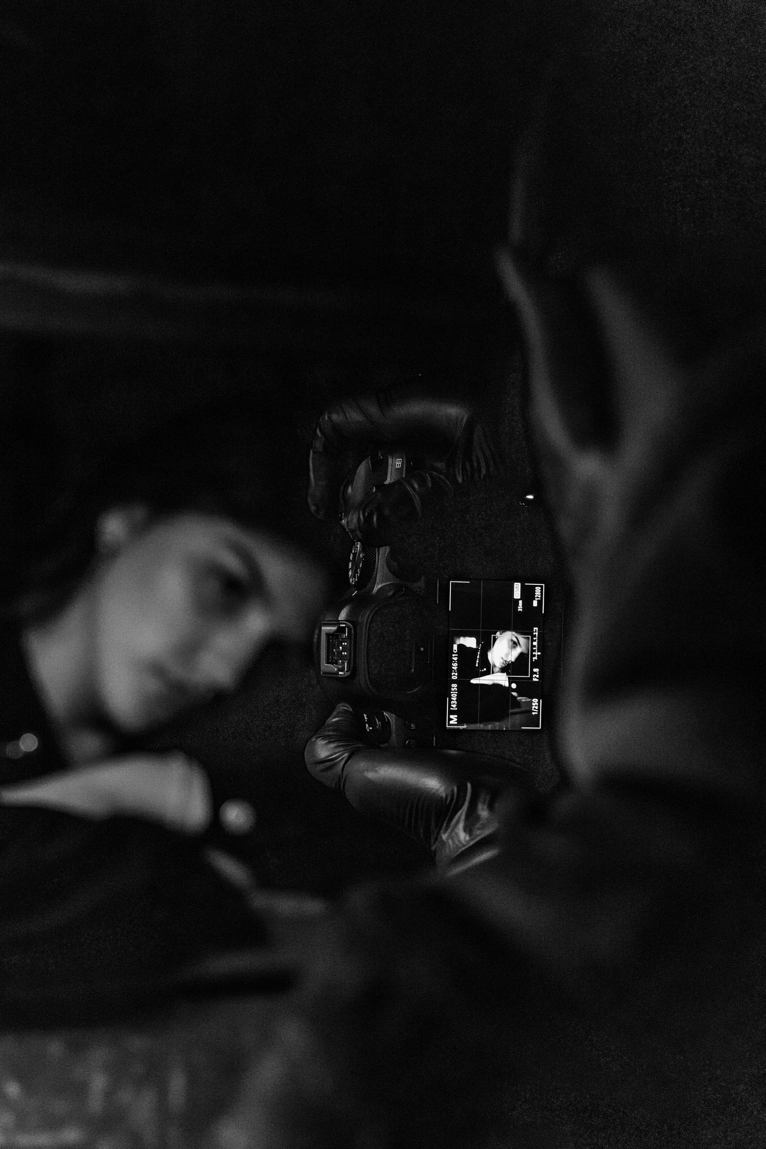 Black and white photo of photographer capturing portrait of woman lying down in dark setting.