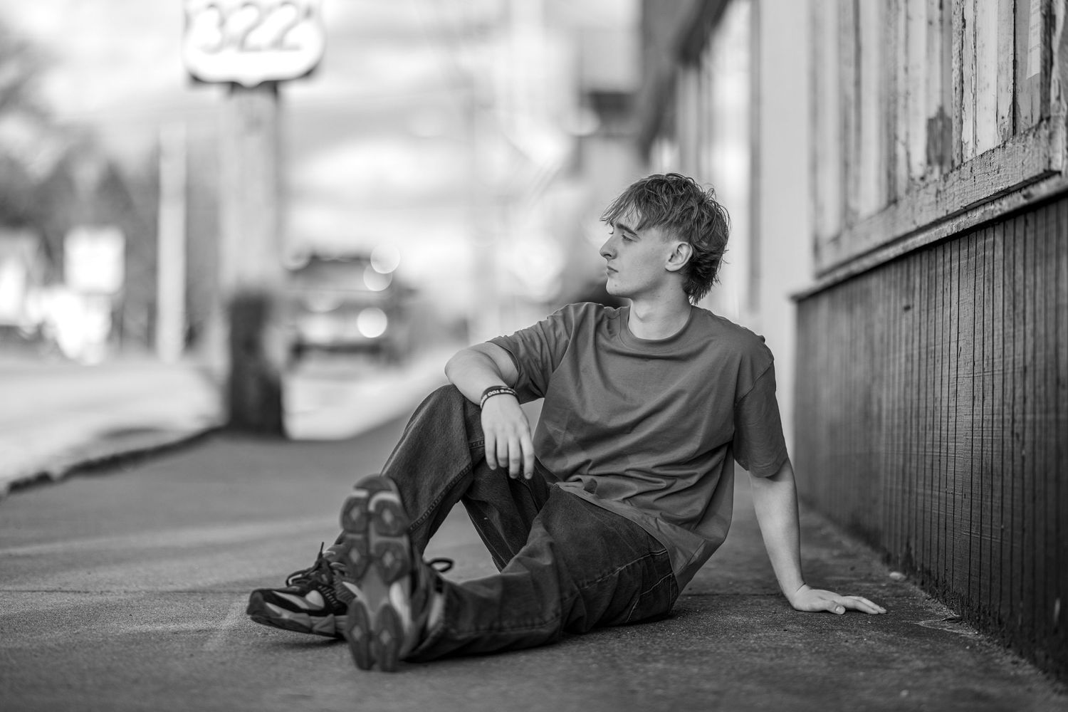 Young man relaxes on city sidewalk in black and white portrait photo.