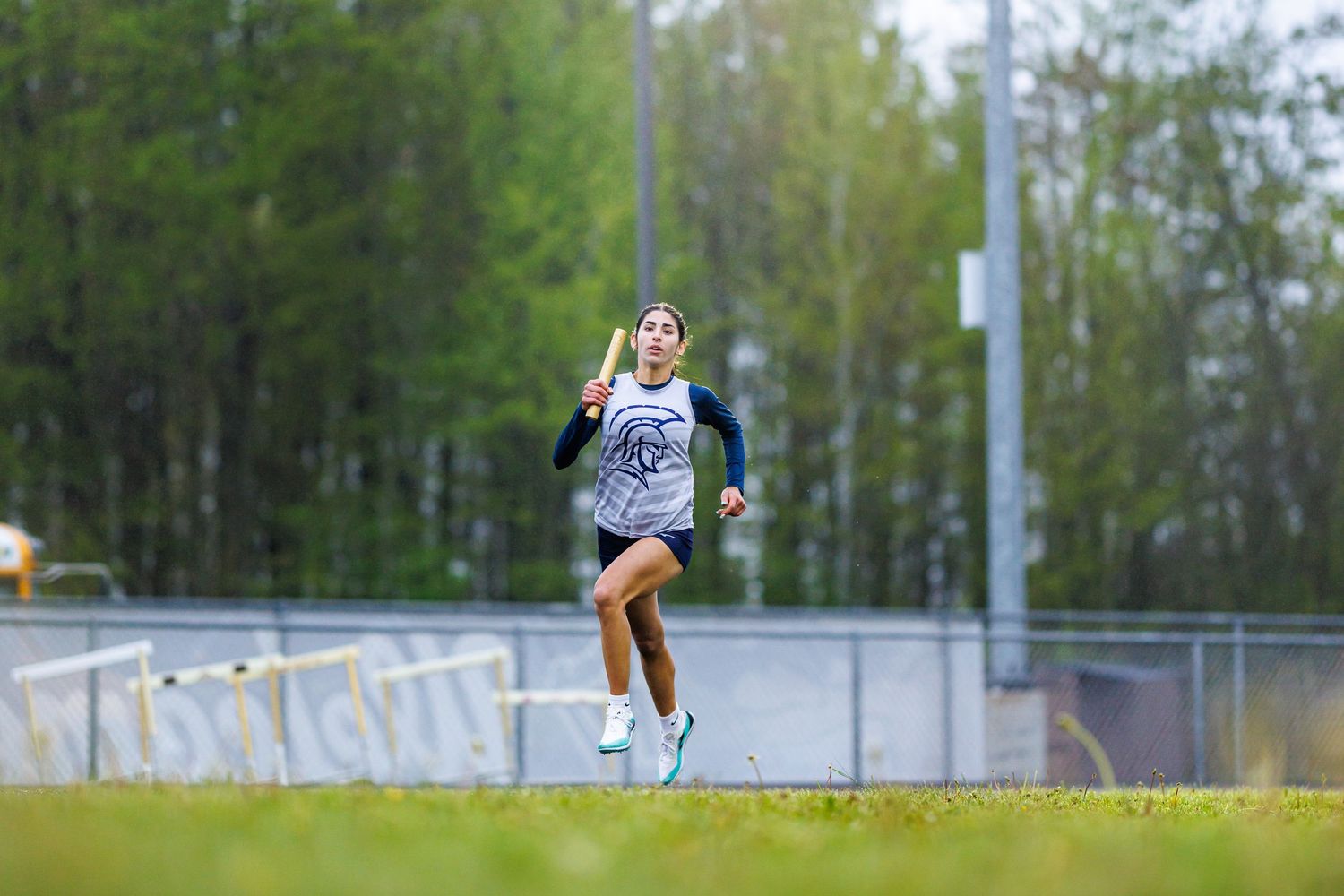 Female athlete running on a track while carrying a pole vault pole.