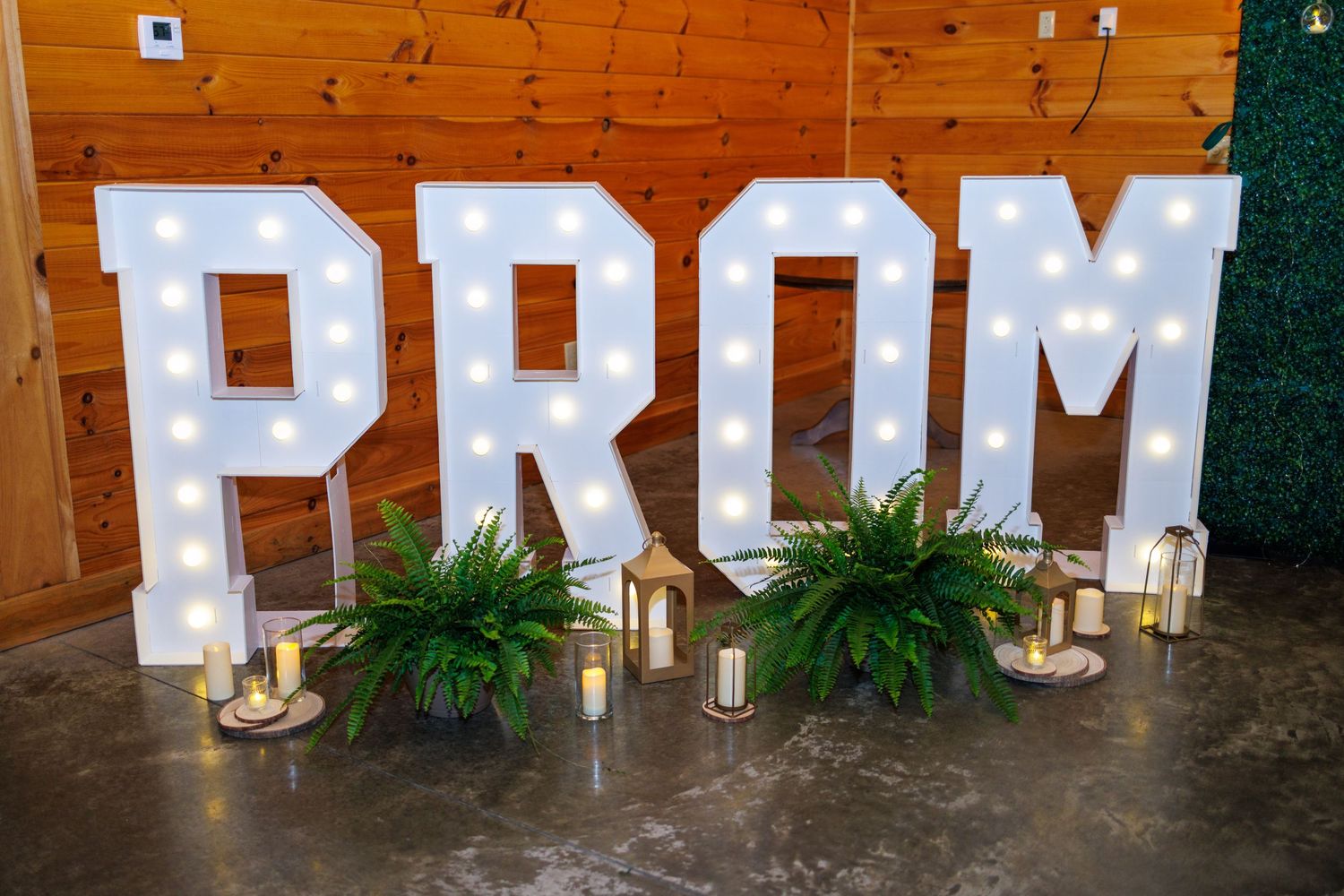 Illuminated marquee letter PROM sign with candles and greenery displayed at a school prom venue.