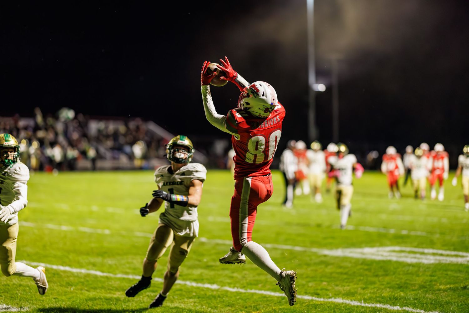 A wide receiver in a red jersey leaps to make a spectacular catch during a night football game.