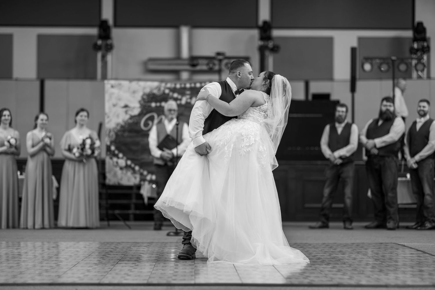 A groom lifts his bride during their first dance at a wedding reception in black and white.