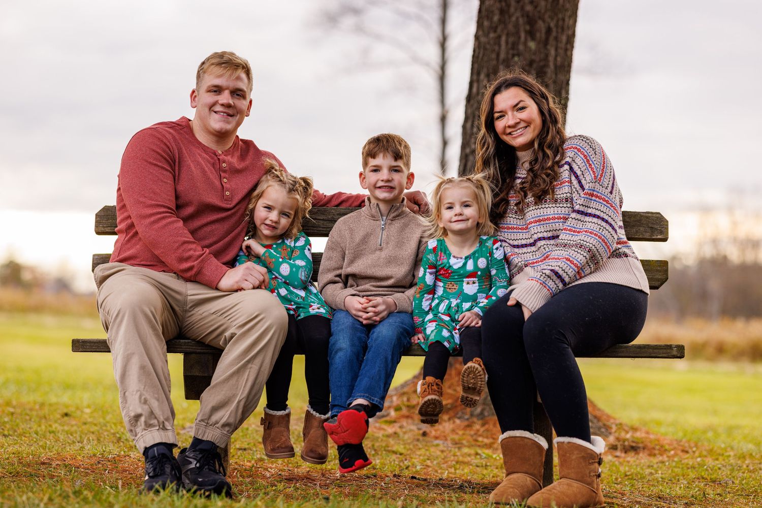 Family of five sitting on a park bench surrounded by fall foliage on an overcast day.