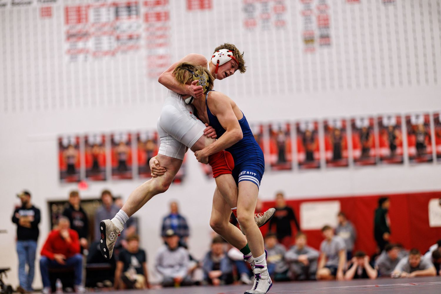 Two wrestlers compete in an intense match, with one athlete lifting his opponent off the mat.