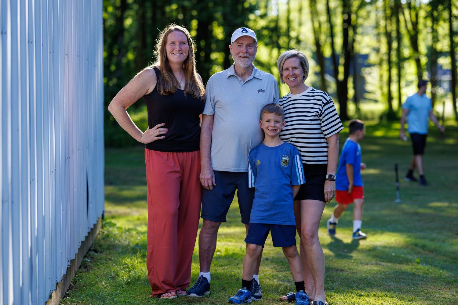 Family of five posing together outdoors near a white building on a sunny summer day.