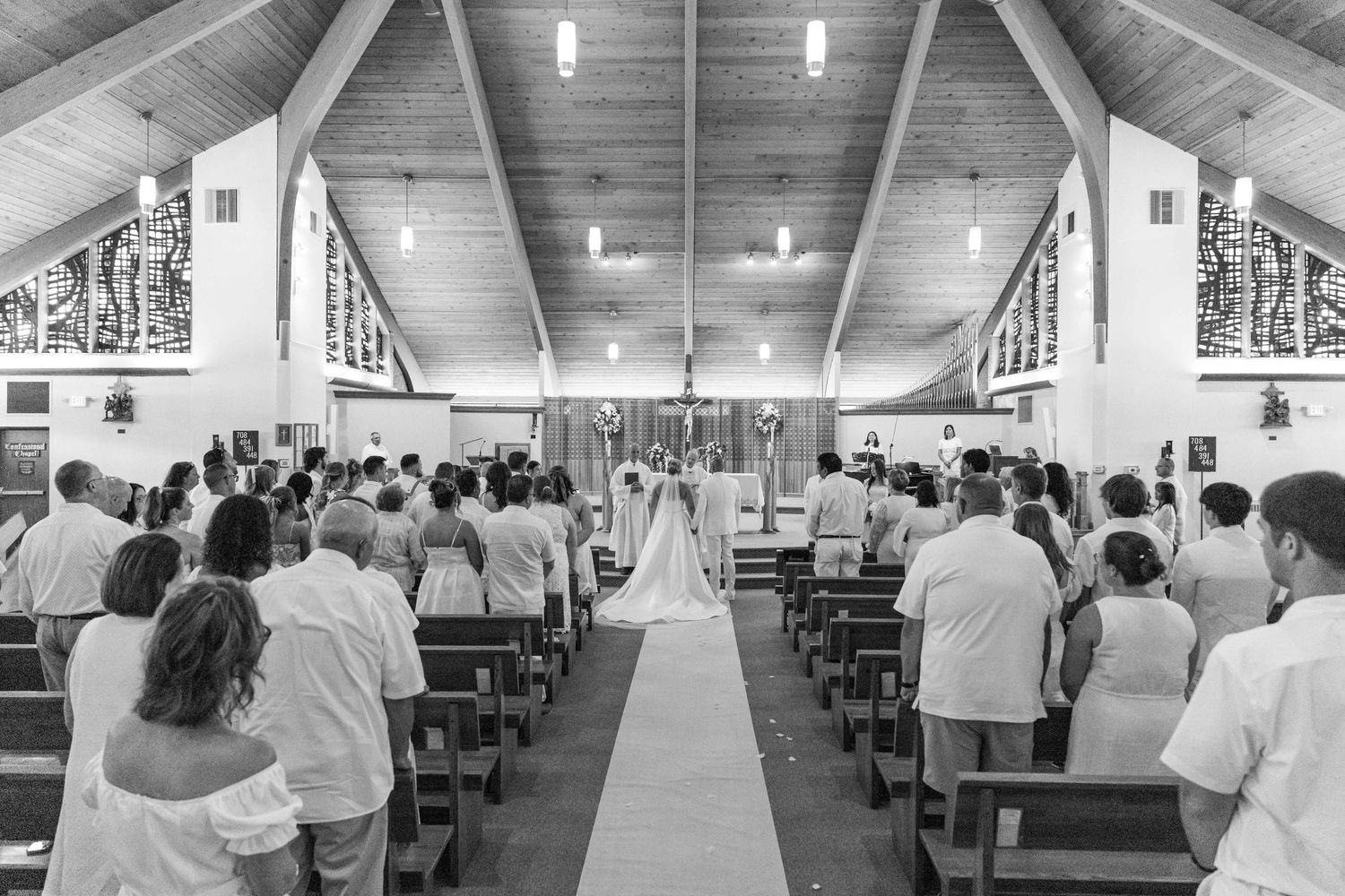 Wedding ceremony in church with guests standing in pews in black and white.