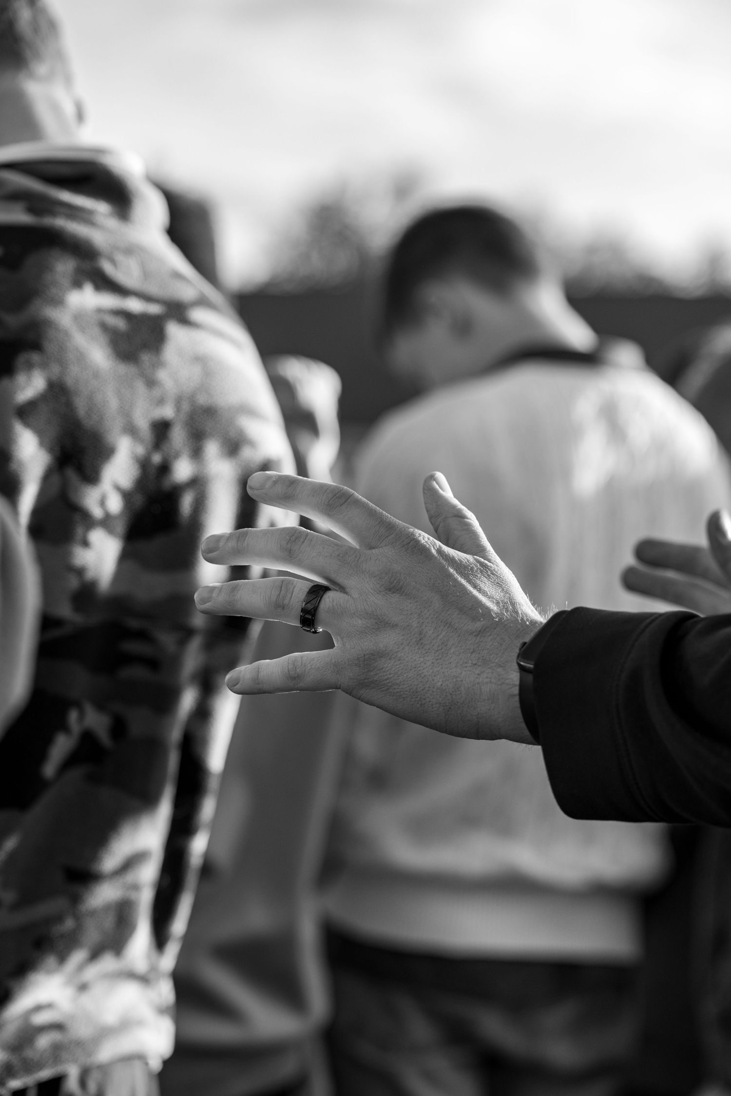 A hand reaches out toward a group of people praying together outdoors.