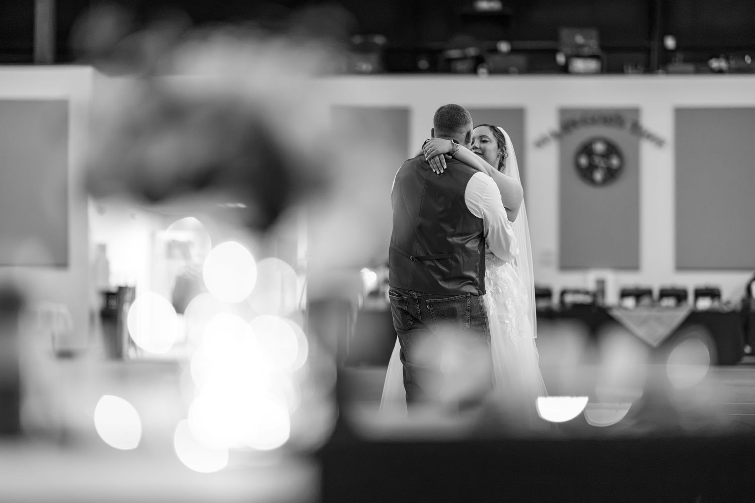Bride and groom dancing at reception with bokeh lights in black and white.