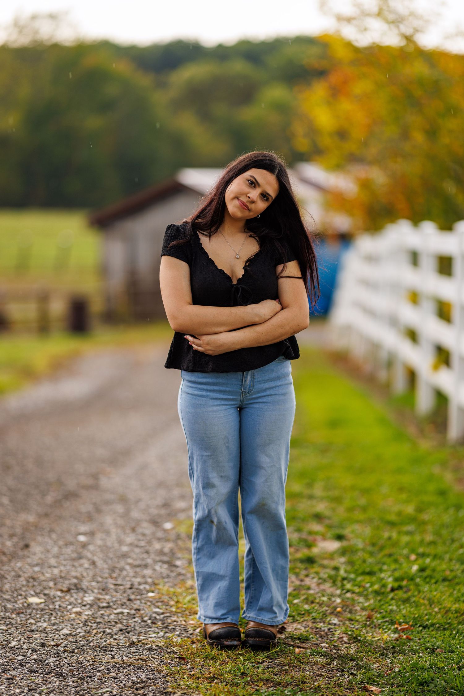 Young woman in black top and jeans standing on gravel farm path in autumn.
