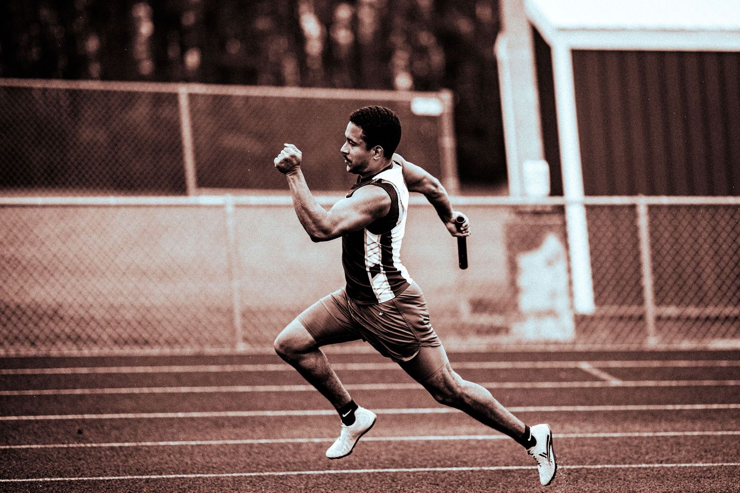 Athlete sprinting on a track holding a relay baton during a race.