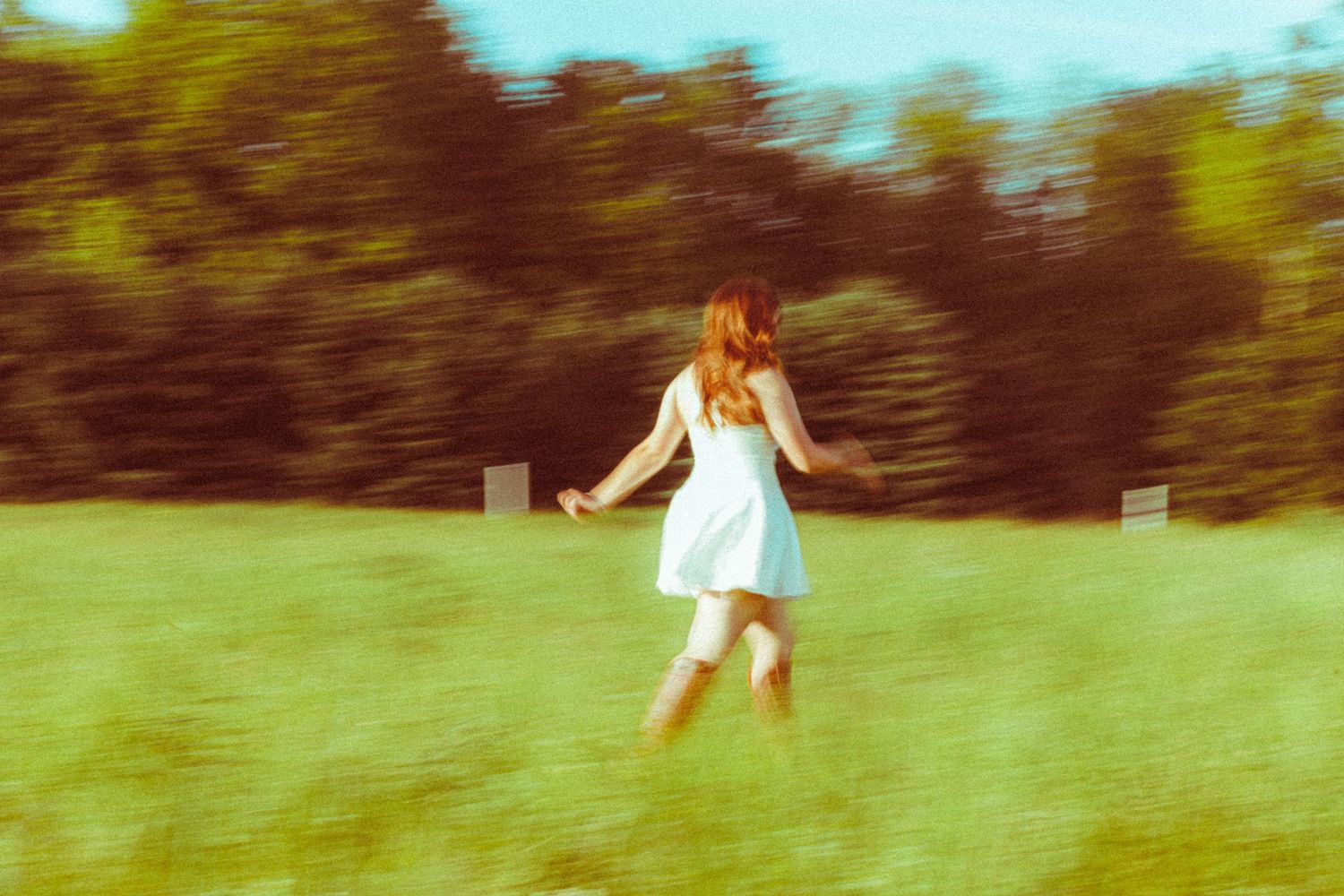 A young woman in a white dress runs through a lush green field, captured with motion blur effect.