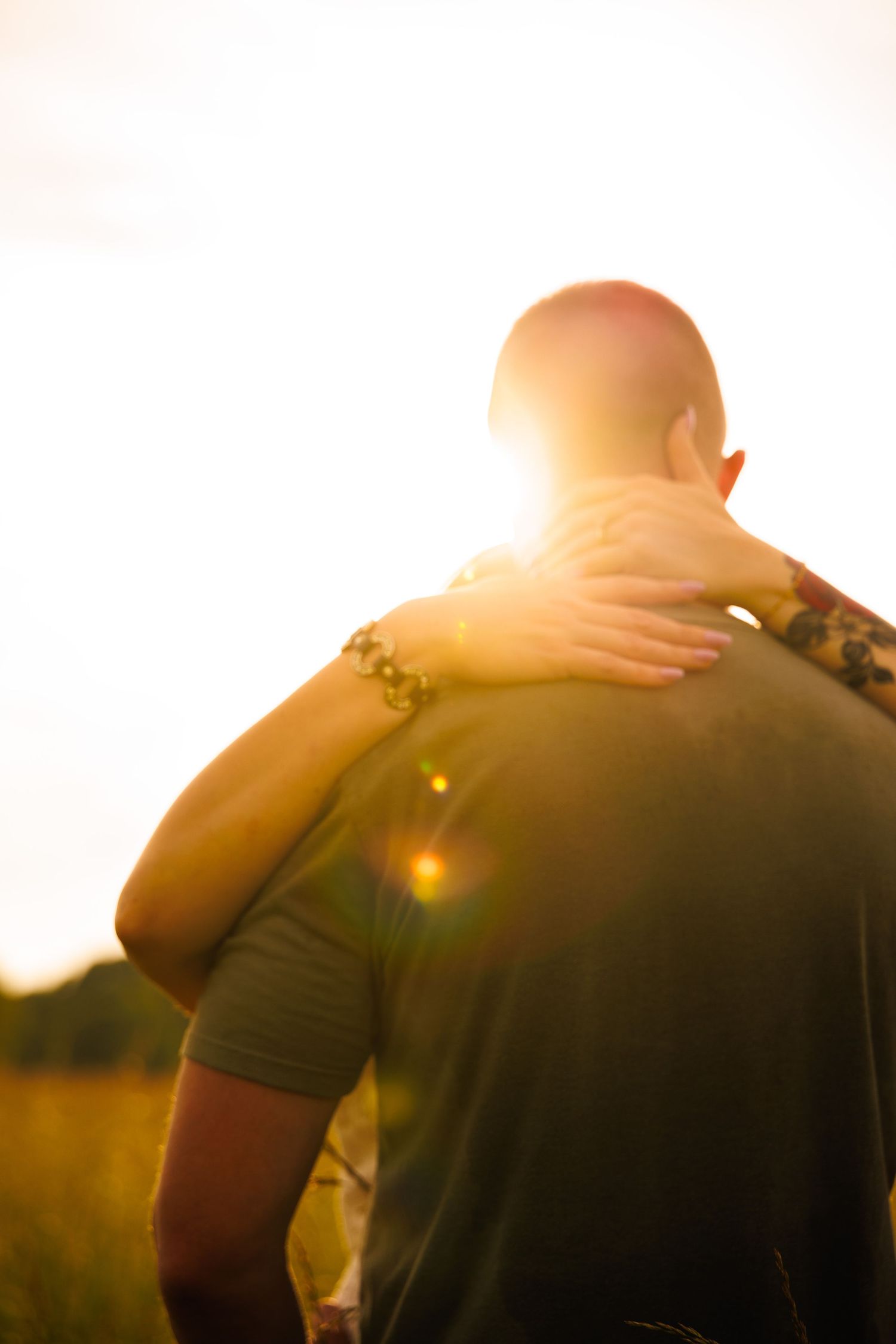 A person rests their hand on a man's shoulder during a golden sunset in an open field.