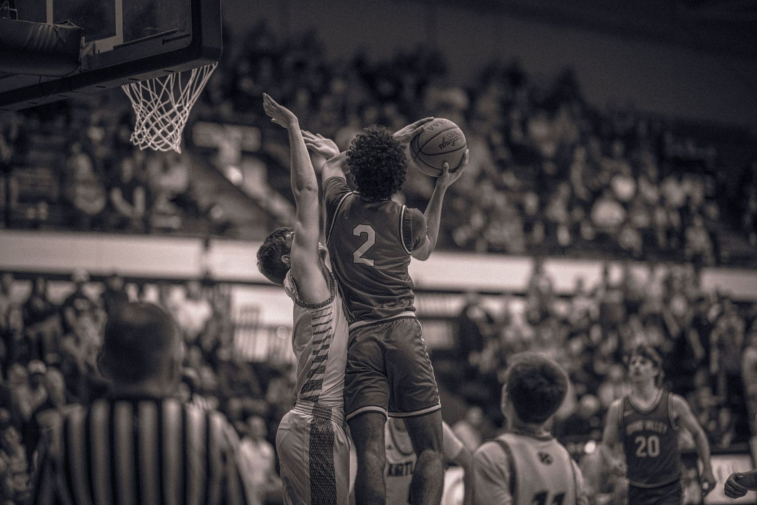 Basketball player driving to the hoop against defenders in a crowded arena.