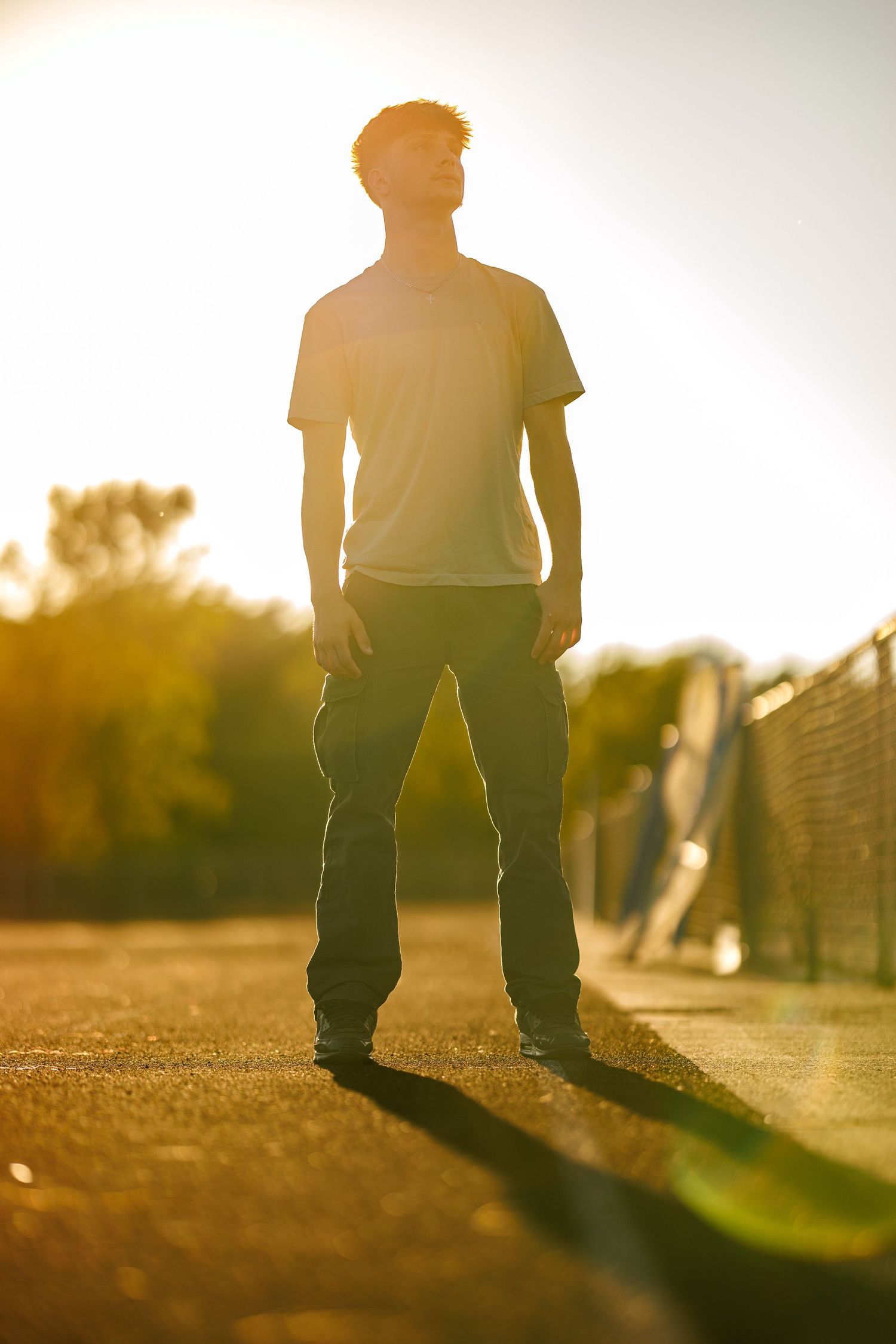 Young man standing in dramatic golden backlight on an outdoor path at sunset.