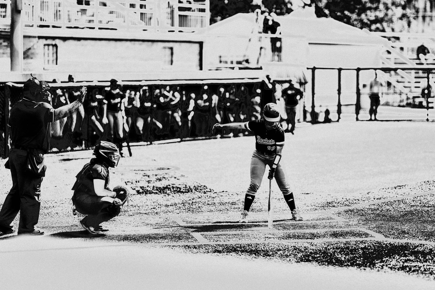A batter prepares to swing at home plate with catcher crouching behind in black and white softball game photo.