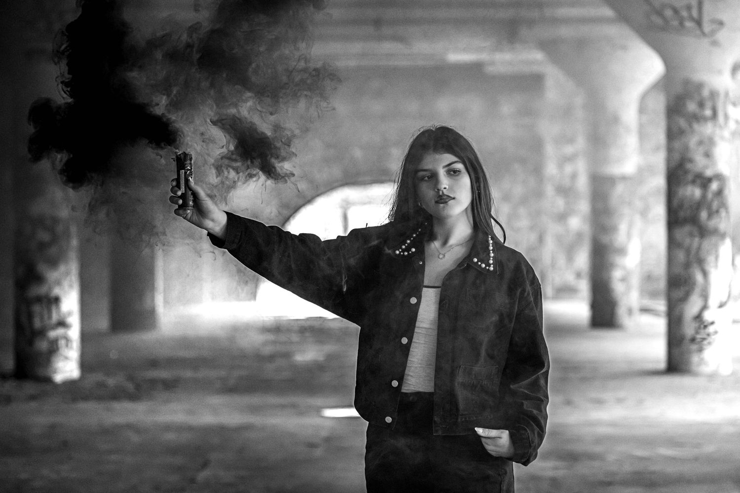 Young woman holds smoke grenade in black and white photo in graffiti tunnel.