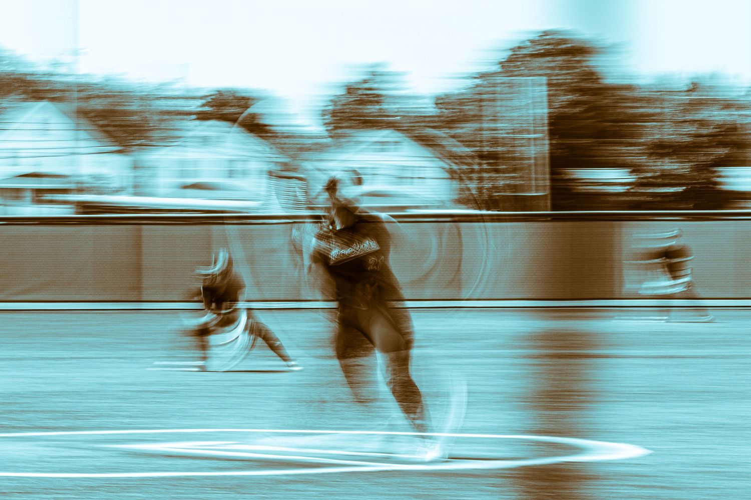 A dynamic motion-blurred cyan-toned photo captures softball players in action during an exciting play at the base.