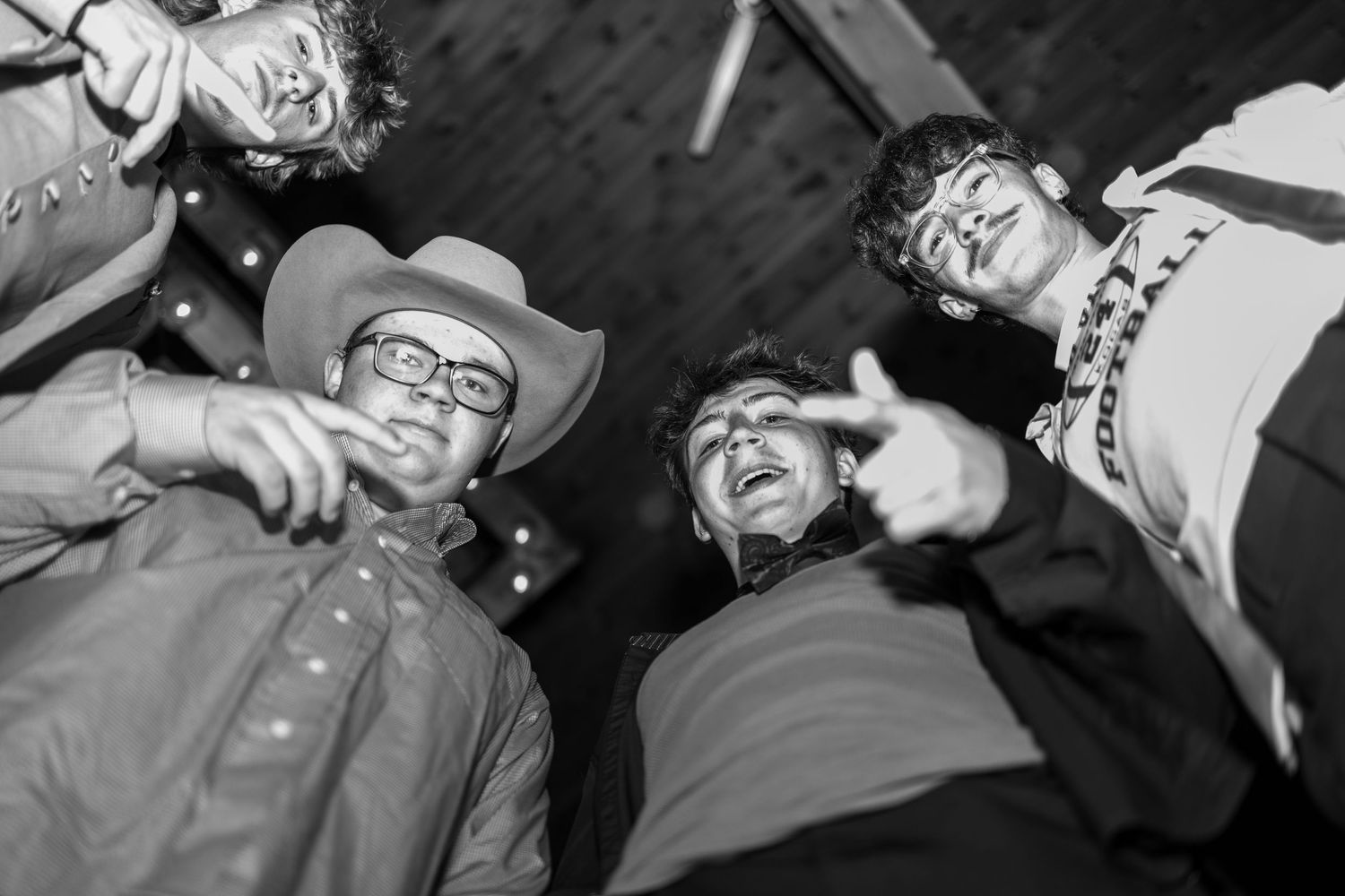 Black and white photo of four young men laughing together at a prom event viewed from below.