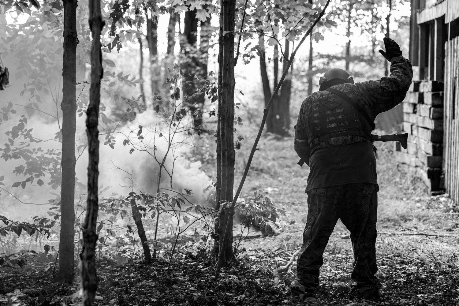 Black and white photo of airsoft player signaling near smoky woodland combat zone.