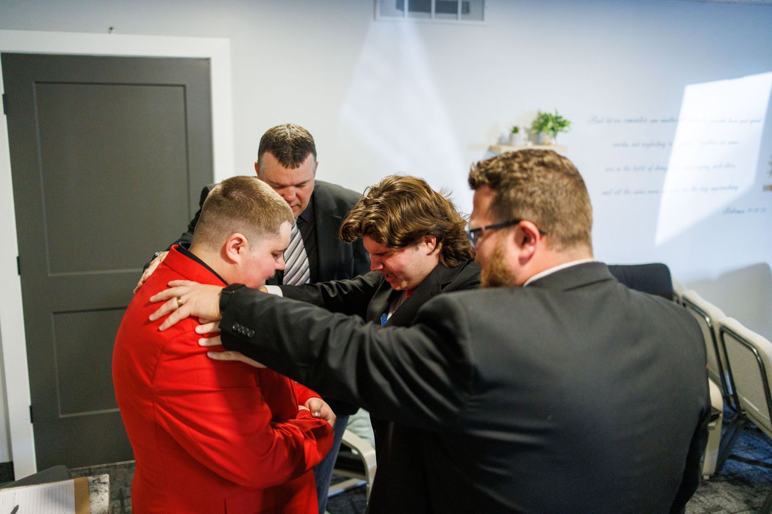 Group of men in formal attire gathered in a circle sharing a prayer before a wedding ceremony.
