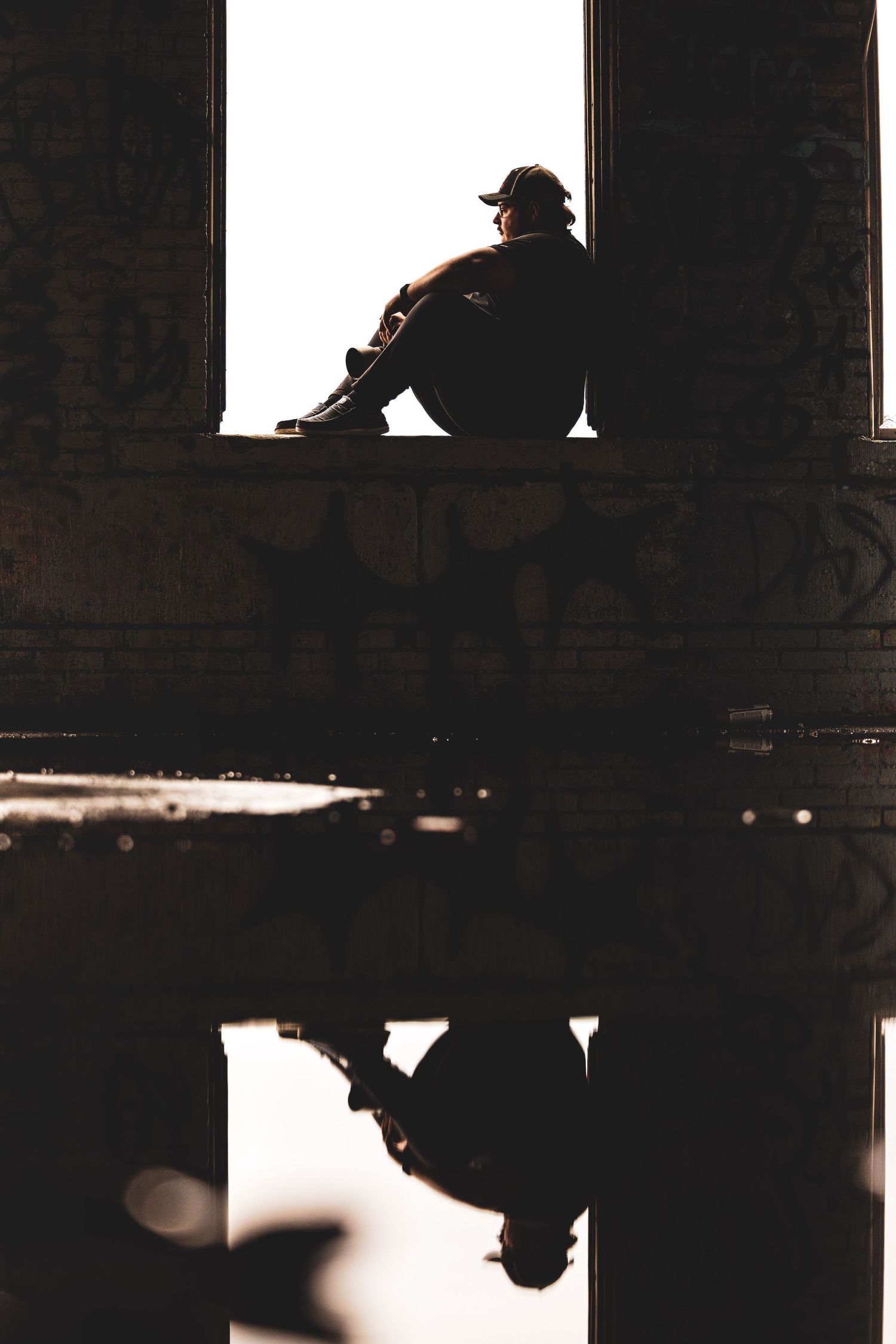 Silhouette of person sitting in doorway reflected in water below in dramatic light.