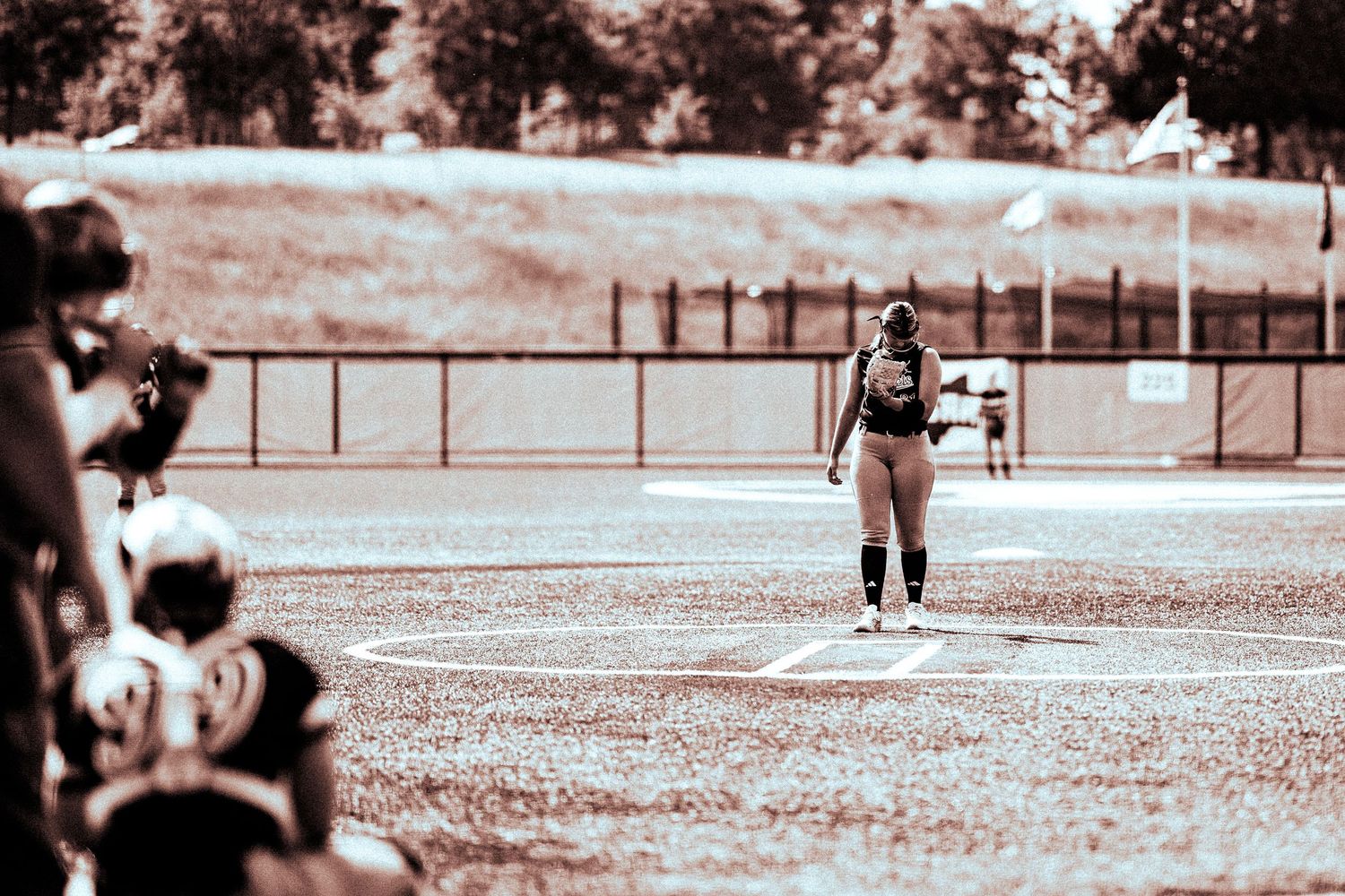A softball player stands ready at base on a vintage-toned sepia field during a competitive game.