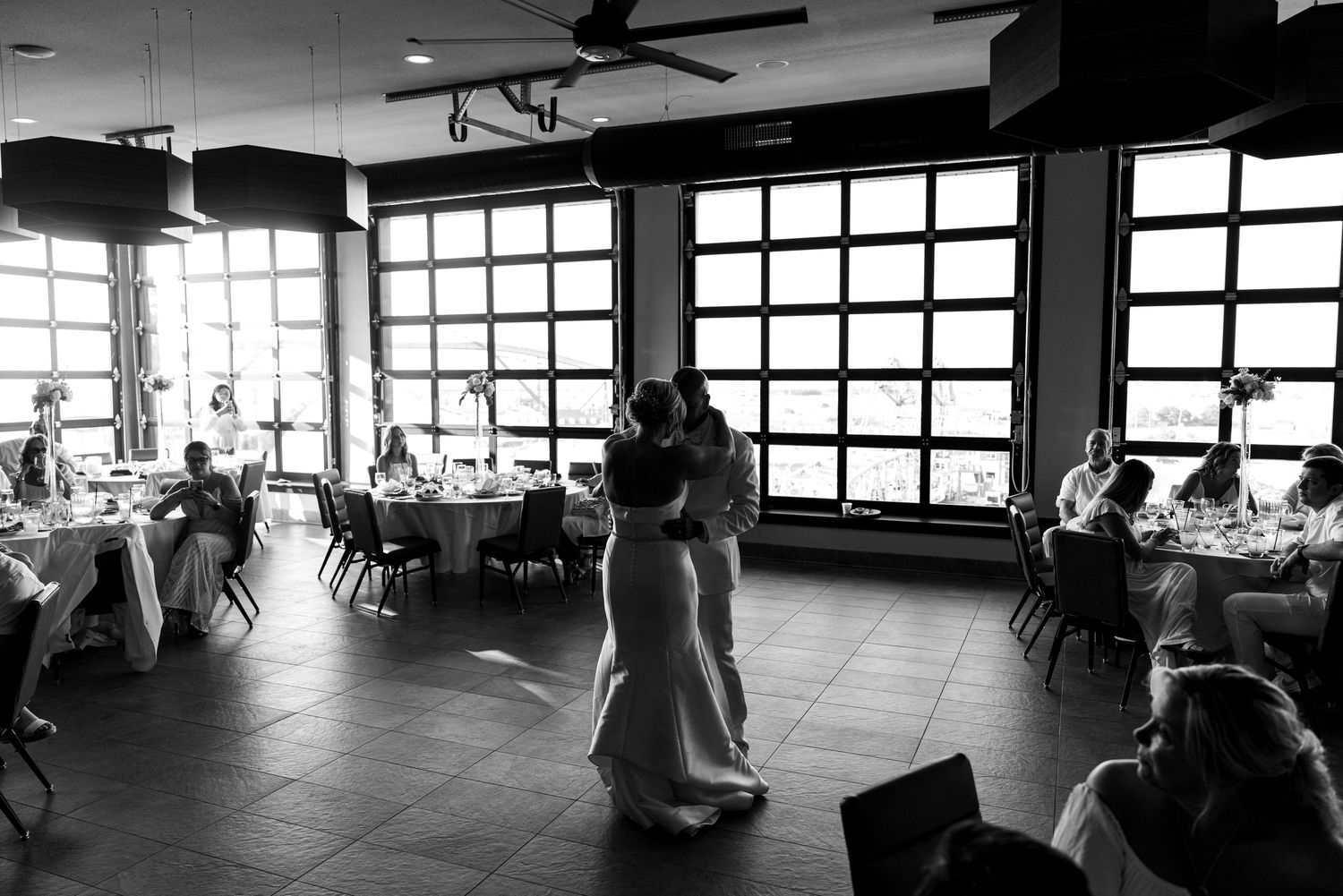 Bride and groom share their first dance in a spacious reception hall with large windows.