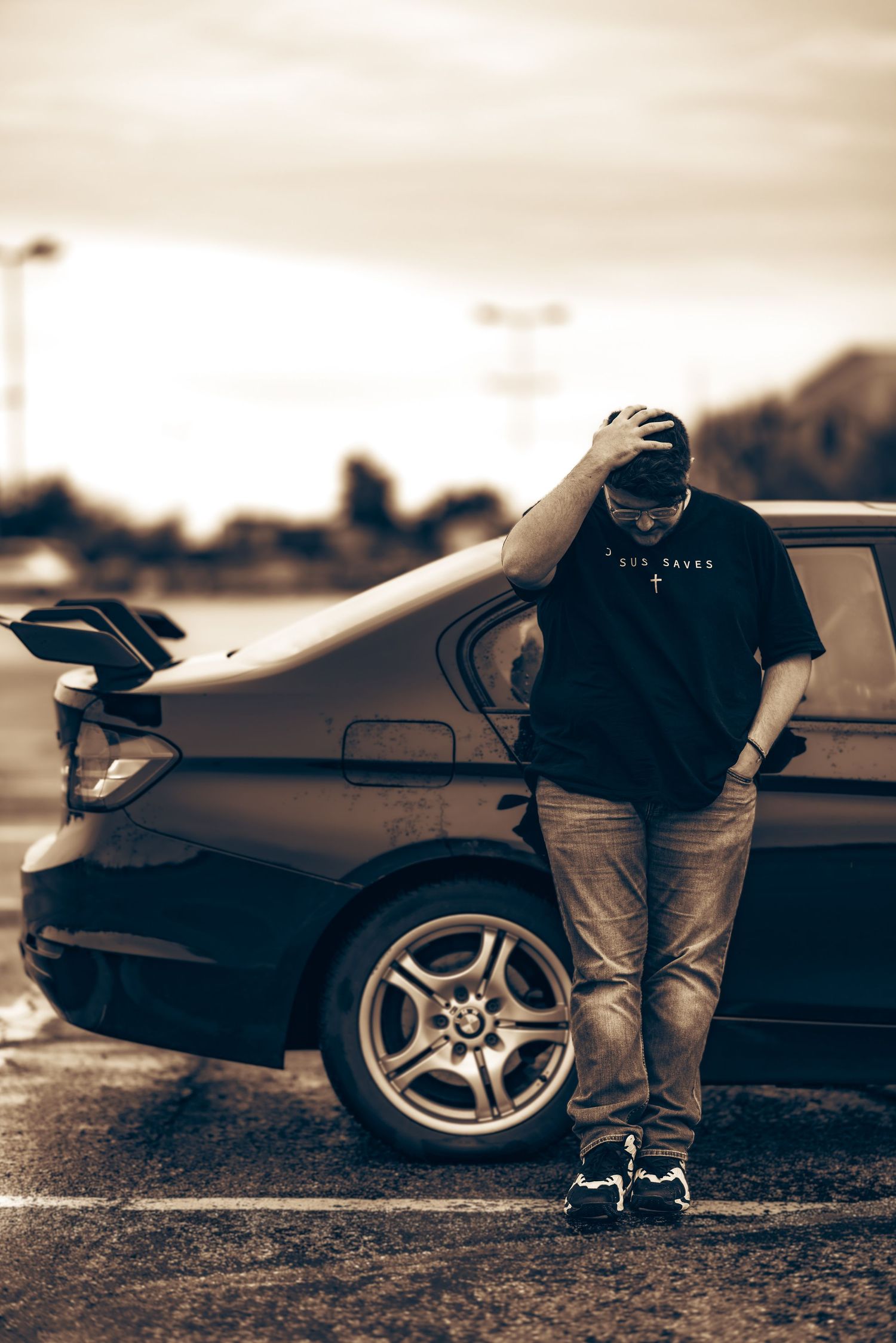 Young man in black tee leaning against a dark BMW car in a sepia-toned portrait photo.